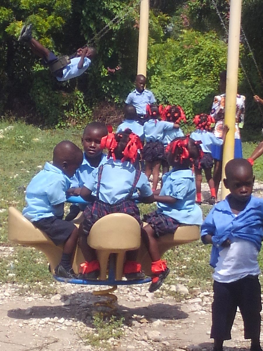Young students seated at desks set up outdoors under the trees