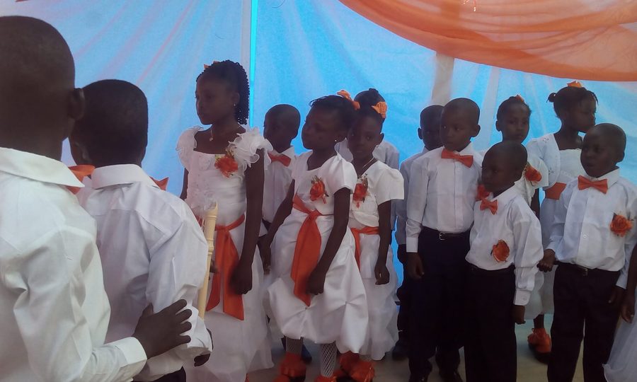 Kindergarten graduates in white shirts and dresses with orange bows, standing together