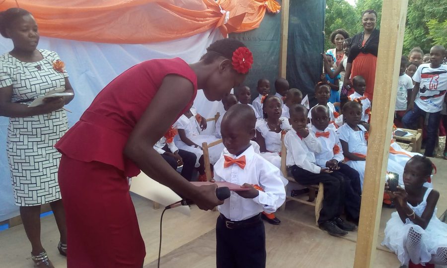 A teacher bending down to hand a young graduate his certificate