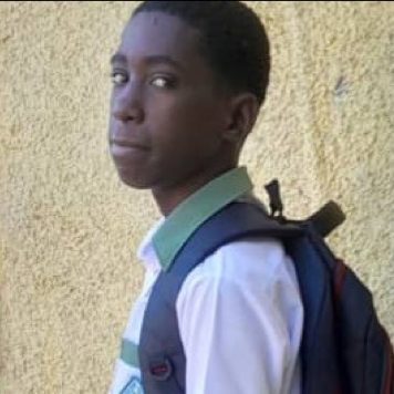 Bensley, a student in school uniform with a backpack, standing against a wall